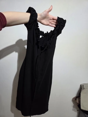 Svart omlottklänning från NLY Trend - Supersnygg svart omlottklänning från NLY Trend i storlek S. Klänningen har volangdetaljer vid ringningen och korta puffärmar med resår. Tillverkad i mjuk bomull som känns skön mot huden. Perfekt för dig som gillar en enkel men trendig look.