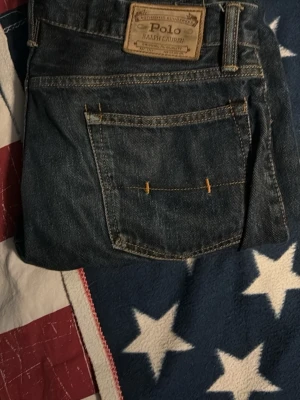 Mörkblå jeans från Polo Ralph Lauren - Snygga mörkblå jeans från Polo Ralph Lauren med klassisk femficksdesign och tydliga kontrastsömmar. Jeansen har en rak passform och är tillverkade i slitstarkt denimtyg med en läderpatch bak i midjan. Perfekta för dig som gillar tidlös stil. 