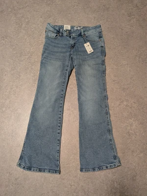 Bootcut jeans med broderade fickor - Super Low Rise Bootcut jeans i ljusblå tvätt från Lager 157, med snyggt broderade bakfickor i guldtråd. Klassisk femficksmodell och normal passform. Jeansen är tillverkade i bomull och har en  Paris embroidery-detalj på baksidan. Storlek M ( 29"-30")