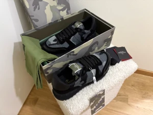Valentino Garavani Rockrunner sneakers - Snygga Valentino Garavani Rockrunner sneakers i svart och grått med camouflage-mönster. Skorna har snörning, rund tå och platt sula. Materialmix av mesh och skinn ger en cool och modern vibe. Kommer med originalkartong och tags. (Finns 2 par)