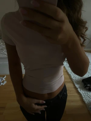 Ljusrosa croppad tajt t-shirt - Säljer en ljusrosa croppad t-shirt med korta ärmar. Toppen har en enkel och stilren design, perfekt att matcha med jeans eller kjol. Materialet känns mjukt och bekvämt mot huden. Passformen är tight och framhäver midjan.