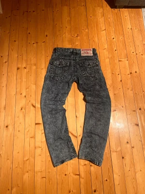 True Religion jeans - Säljer ett par blåa acid wash jeans från True Religion med ikoniska bakfickor och detaljerade sömmar. Modellen har raka ben och klassisk femficksdesign. Jeansen är ovanliga!
