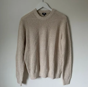 Beige stickad tröja från Uniqlo - Säljer en beige stickad tröja från Uniqlo i storlek L. Tröjan har grovstickad struktur, rund hals och ribbade muddar vid ärmslut och nederkant. Materialet är en mix av bomull och akryl, vilket gör den både mjuk och skön. Perfekt för dig som gillar enkel och clean stil. 5K6