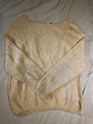 Beige stickad tröja med paljetter - Snygg beige stickad tröja med glittriga paljetter och långärmad modell. Baksidan har en öppning med satinband som knyts i nacken för extra detalj. Perfekt för dig som gillar lite extra bling och mjuka material.