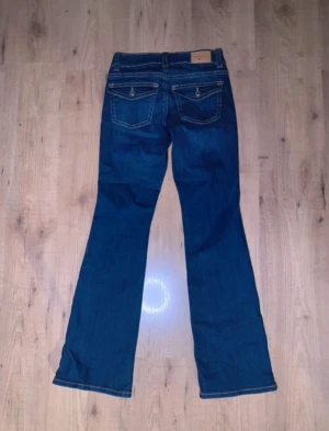 Blå bootcut jeans från Levis - Säljer ett par klassiska blå Levis jeans med bootcut passform och låg midja. Jeansen har snygga kontrastsömmar, fem fickor och detaljerade bakfickor med lock och knapp. Materialet är slitstarkt jeans och modellen sitter tajt över höften och låren innan de blir vidare nedtill.