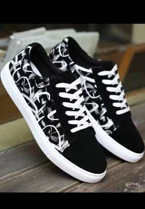 Svarta sneakers med vit graffiti - Svarta sneakers med vit graffiti-inspirerat mönster och vita snören. Skorna har en platt vit sula och rund tå. Materialet ser ut att vara syntet med textilinslag, vilket ger en cool och urban vibe. Perfekt för dig som gillar streetstyle och vill sticka ut.