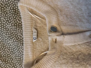 Beige stickad kofta med knappar - Mysig beige stickad kofta från C med rund halsringning och snygga silvriga knappar framtill. Koftan har långärmad passform och ribbade muddar vid ärmslut och nederkant. Perfekt för lager-på-lager under kyliga dagar.