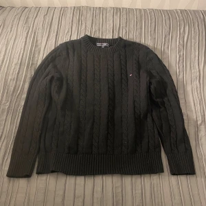 Svart kabelstickad tröja Tommy Hilfiger - Svart kabelstickad tröja från Tommy Hilfiger i storlek M. Tröjan har rund hals, ribbade muddar och ett litet broderat logomärke på bröstet. Perfekt för dig som gillar klassisk stil med snygga detaljer och vill ha något som funkar året runt. Har krymt pga tvätt så mer åt S hålet.