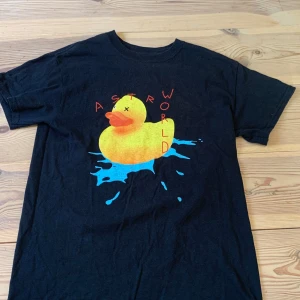 Astroworld svart t-shirt med tryck - Svart Astroworld t-shirt i bomull med färgglatt tryck av en gul badanka och texten 'ASTROWORLD' på framsidan. Baksidan har neonfärgad grafik med 'Wish You Were Here' och 'Europe 2019 World'. Perfekt för dig som gillar streetwear och Travis Scott.