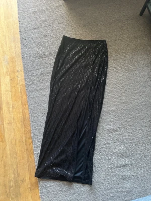 Svart långkjol med paljetter och slits - Säljer en svart långkjol med glittriga paljetter och slits på sidan. Perfekt för dig som vill sticka ut med lite extra glitter under kommande party season! 