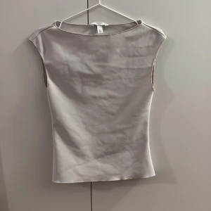 Beige topp från H&M - Säljer en stilren beige topp från H&M med rund hals och ärmlös design. Toppen har en mjuk och slät yta, perfekt för att skapa en clean look. Passformen är normal och materialet känns lätt mot huden.
