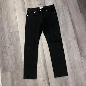 Svarta jeansbyxor från 157, straight - Svarta jeansbyxor från 157 med klassisk femficksdesign och raka ben. Modellen heter New Classic och har en stilren look med svarta nitar och knapp. Passar dig som gillar enkel och clean stil. Materialet är jeans och midjan är normal.
