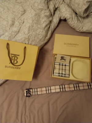 Burberry bälte med klassiskt rutmönster - Säljer ett snyggt Burberry bälte med ikoniskt rutmönster i beige, svart och vitt samt en elegant metallspänne med Burberry-logga. Bältet är tillverkat i skinn och levereras med originalförpackning och påse. Perfekt accessoar för att lyfta din outfit.