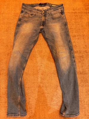 Replay Anbass blå jeans - Snygga Replay Anbass jeans i klassisk blå tvätt. Slim fit-modell med fem fickor. Bakfickorna har Replay-logga och jeansen är tillverkade i stretchigt bomullsmaterial för skön passform. Skick 7/10 pga en liten slitning precis nedanför gylfen men inget som syns om man inte vet om det. Storlek 31/30! 