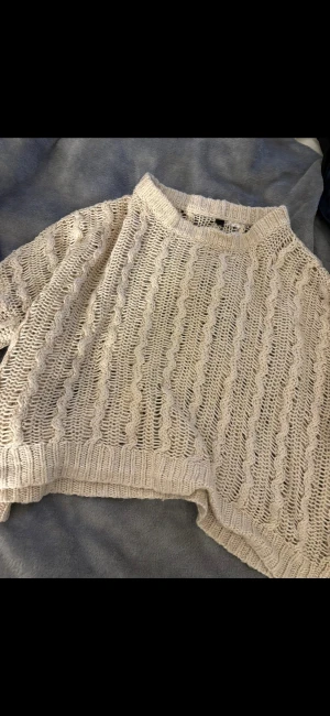 Beige stickad tröja med kabelmönster - Säljer en beige stickad tröja från H&M med grovt kabelmönster och luftig struktur. Tröjan har långärmade ärmar, ribbad hals och muddar. Perfekt för lager-på-lager och chill stil. Passar dig som gillar en loose fit och mysiga vibes. den är croptop alltså kort på, och man har den över en tröja