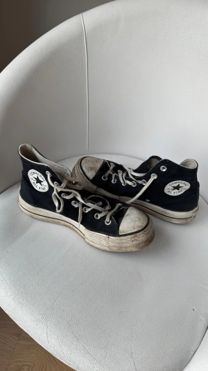 Svarta Converse All Star sneakers - Svarta Converse All Star high-top sneakers med vit rund tå och platt sula. Klassisk logga på sidan, vita snören och kontrasterande vita detaljer. Tillverkade i textil med gummisula. Perfekt för dig som gillar retro och streetstyle.