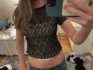 Svart spetsig croppad blus - Säljer en svart, croppad blus i spets med korta ärmar. Toppen har ett genombrutet mönster och kan bäras både med vanlig halsringning eller offshoulder. 