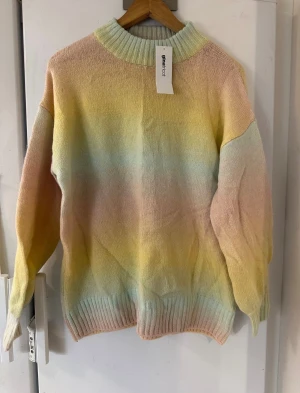 Ny Gina Tricot tröja st. XS - En Superfin ny stickad tröja från Gina Tricot i mjuka pastellfärger som går i ljusgul, ljusblå, ljusrosa och beige. Tröjan har en ribbad, hög hals och ribbade muddar vid ärmslut och nederkant. Perfekt för dig som gillar färg och vill ha en mysig look. En stickad tröja med inslag av ull (8%). Den är overzised och passar upp till st.L  Modell: Marianne Knitted Sweater  48% akryl, 24% polyamid, 18 polyester, 8% ull, 2 % elastan