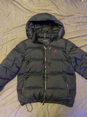 Mörkblå Ralph Lauren dunjacka - Mörkblå dunjacka från Polo Ralph Lauren i storlek M, köptes förra året på NK för runt 5000kr och har bara används under den vintern. Om du har frågor är de bara att fråga!