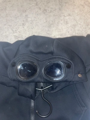 C.P. Company - Säljer en svart C.P. Company med glasögon i luvan!  Mycket skön och mycket fin tröja i mycket bra skick! Detta är en gammal modell. Vid frågor eller annat är det bara att skriva!✍️ 