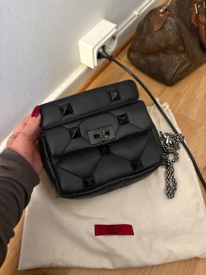 Valentino Gravani Rockstud väska - Säljer min Valentino rockstud gravani väska. Den svarta färgen på metallen på väskan har gått av lite så har målat över de med svart men inget som märks mycket utöver de väldigt bra skick! Väskan har gått igenom en äktahetskoll från vestaire collectiv som anges på sista bilden! •Faktisk bredd: 19.5 cm/7.48 tum  • Faktisk höjd: 16 cm/6.30 tum  • Verkligt djup: 6 cm/2.36 tum   