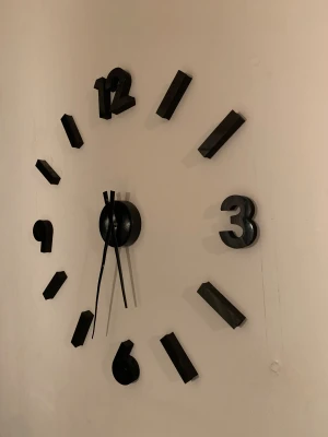 Svart väggklocka med 3D-siffror - Säljer en stilren svart väggklocka med stora 3D-siffror och minimalistisk design. Klockan har svarta visare och siffror i plast som monteras direkt på väggen, vilket ger en modern och cool look till rummet. Perfekt för dig som gillar grafisk och enkel inredning.