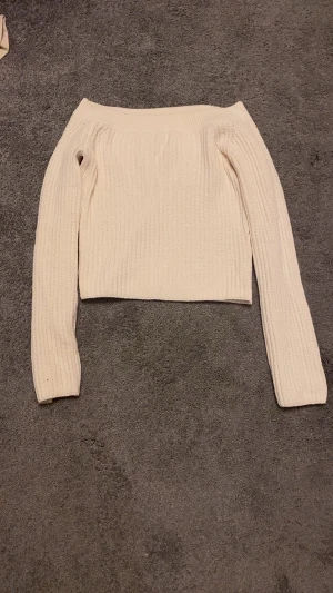 Offshoulder ribbad stickad tröja - Snygg offshoulder stickad tröja i ljus beige färg. Tröjan har ribbad struktur och långa ärmar, perfekt för dig som gillar en enkel men trendig look. Passar dig som vill ha en croppad stil och gillar mjuka material.