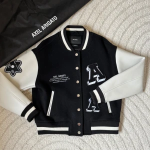Illusion Varsity Jacket Black Axel Arigato - Säljer denna rejäla collegejackan från det stilrena märket Axel Arigato! Slutsåld på deras egna sida där den köptes ifrån, men säljs vidare utav andra för ungefär 4500 kr. Jackan är som sprillans ny och har inga tecken på användning⭐️Jackan är herrmodell men ger en snygg oversize look för mig. Den har skinn ärmar med en ullkropp, så perfekt nu till hösten. Och självklart är den äkta!