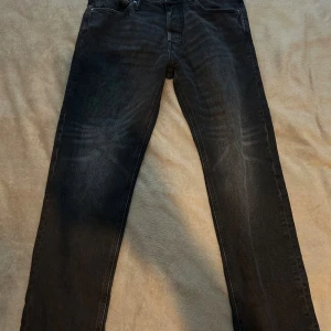 Svarta jeansbyxor från Jack & Jones - Snygga svarta jeansbyxor från Jack & Jones med klassisk femficksdesign och raka ben. Jeansen har en något tvättad look och är tillverkade i mjukt denimtyg som sitter skönt hela dagen. Perfekta för dig som gillar en stilren och enkel look.