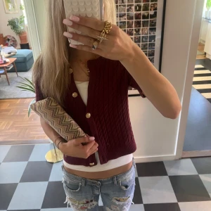 Vinröd kortärmad kofta med guldknappar - Kortärmad vinröd kofta från H&M med kabelstickat mönster och snygga guldknappar framtill. Storlek M💋💋