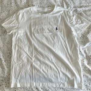 Vit t-shirt från Polo Ralph Lauren - Vit t-shirt från Polo Ralph Lauren i bomull med klassisk broderad logga på bröstet. Modellen är slim fit och har korta ärmar och rund hals. Perfekt basic-plagg med clean look och snygg passform.