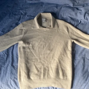 Ljusbeige merinoulltröja från These Glory Days - Klassisk ljusbeige långärmad merinoulltröja från These Glory Days i mjuk superior merinoull. Tröjan har en stilren krage och ribbade muddar vid ärmslut och nederkant. Perfekt för vardagar och chillkvällar. Den har mycket bra skick utan nopper och defekter. 