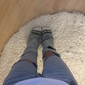 Ljusblå slitna jeans med broderade fickor - Säljer ett par ljusblå jeans med stora slitningar över knäna och broderade detaljer på bakfickorna. Jeansen har rak passform och klassisk femficksdesign. Perfekta för dig som gillar en avslappnad och trendig look. Jag har klippt två nya hål i dem .pris kan diskuteras