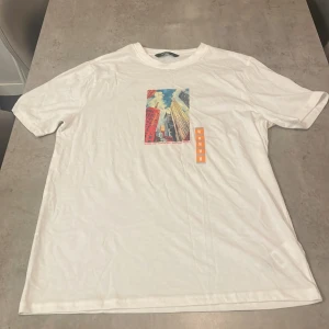 Vit t-shirt med citymotiv från Xside - Vit t-shirt från Xside i bomull med tryck av höga skyskrapor och texten 'Where city lights meet restless nights' på bröstet. Klassisk rund hals och korta ärmar. Perfekt för dig som gillar urban stil och snygga prints.