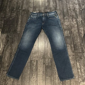 Replay Anbass jeans blå 31/30 - Snygga Helt Nya Replay Anbass jeans i klassisk blå tvätt med lätt slitning. Modellen är Anbass i Replay, fem fickor och tydliga kontrastsömmar. Tillverkade i återvunnet jeansmaterial för en schysstare stil. Perfekta för dig som gillar en tidlös look med modern touch. Nypris: 1799