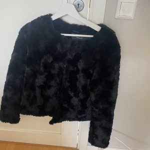 Svart pälsjacka från Vero Moda - Mysig svart pälsjacka från Vero Moda i storlek M. Jackan har en fluffig och mjuk känsla, rund halsringning och långa ärmar. Perfekt för att hålla värmen och ge en cool look under kyliga dagar.
