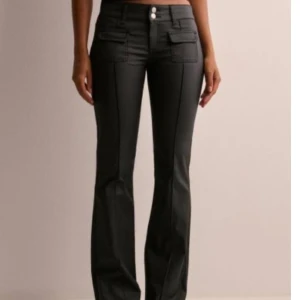 Svarta bootcut byxor med fickor - Aldrig använda.Snygga svarta bootcut byxor med hög midja och markerade sömmar framtill. Byxorna har två stora fickor med lock framtill och dubbla knappar i midjan. Materialet ser ut som skinn eller syntet, vilket ger en cool och trendig look. Nypris: 699kr säljer för 450kr.
