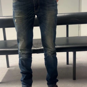 J. Lindeberg jeans - Snygga blå jeans från Levis med skinny passform och klassisk femficksdesign. Jeansen har slitningar och en något tvättad look som ger en cool vibe. Perfekta för dig som gillar en smal siluett och vill ha ett par jeans som sitter tajt hela vägen ner.