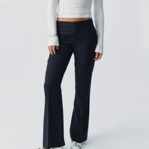 Mörkblå randiga kostymbyxor bootcut - Snygga mörkblå kostymbyxor med vita tunna ränder i klassiskt pinstripe-mönster. Byxorna har bootcut-snitt och sitter midwaist. Perfekta för en stilren och trendig look. Materialet känns dressat och passar till många olika outfits.