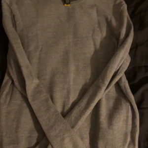 Grå stickad tröja från Polo Ralph Lauren - Snygg grå stickad tröja från Polo Ralph Lauren med rund halsringning och diskret broderad logga på bröstet. Tröjan har långa ärmar och ribbade muddar för en clean och klassisk look. Perfekt för lager-på-lager under kyliga dagar. Väldigt stilren och passad perfekt för vardagen. Säljer denna för bra pris 