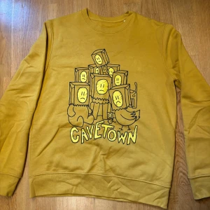Gul Cavetown sweatshirt med tryck - Gul sweatshirt från Cavetown med unikt tryck av figurer med kartonghuvuden och texten 'Cavetown' på framsidan. Tröjan har rund hals, långa ärmar och är gjord i mjuk bomull. Perfekt för dig som gillar coola bandmerch och vill sticka ut. Pruta gärna. 💕