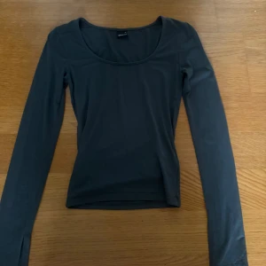 Mörkgrön långärmad topp Gina Tricot XS - En mörkgrön långärmad topp från Gina Tricot i storlek XS. Toppen har en rundad, djup urringning och är figurnära i modellen. Perfekt att styla med jeans eller kjol för en clean och enkel look.