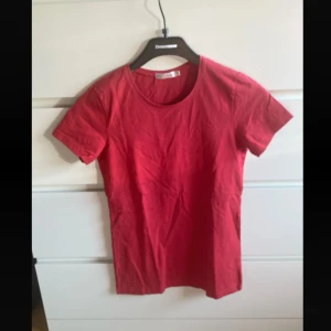 Röd basic t-shirt i bomull - Enkel röd t-shirt med rund halsringning och korta ärmar. Skön och klassisk modell i mjuk bomull, perfekt till jeans eller shorts. Snygg att bära som den är eller under en skjorta.