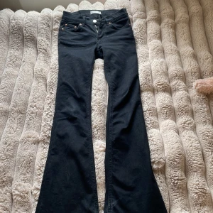 Svarta bootcut jeans från Gina - Svarta jeans från Gina  med klassisk femficksdesign och snygg bootcut-passform. Jeansen har hög midja, dragkedja och knapp framtill samt detaljer i kopparfärg. Materialet är mjukt och stretchigt för en bekväm känsla.