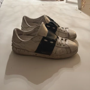 Valentino Open sneakers vit/svart skinn - Säljer ett par Valentino Open sneakers i vitt skinn med bred svart läderdetalj över mitten. Klassisk rund tå, vita snören och platt sula. Märkeslogga på plösen. Snygg och stilren design som sticker ut med den svarta kontrasten.