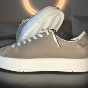 Beige sneakers från Vagabond i mocka - Snygga beige sneakers från Vagabond med ovandel i mocka och vita snören. Skorna har en vit, platt sula och klassisk rund tå. Insidan är fodrad med textil och läder för extra komfort. Perfekta för dig som gillar stilrena och cleana sneakers.