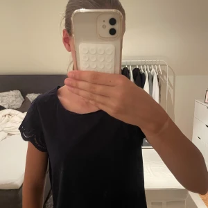 Mörkblå blus med spetsärm Orsay - Supersöt mörkblå blus från Orsay med korta ärmar i broderad spets och rund halsringning. Baksidan har en liten knytning i nacken för extra detalj. Perfekt att styla med jeans eller kjol för en chill look.