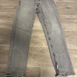 Grå raka jeans från Zara, strl 38 - Grå jeans från Zara i rak modell med normal passform. Jeansen har råa, slitna benslut och klassisk femficksdesign. Tillverkade i denim med snygg tvättad look. Perfekta för dig som gillar en avslappnad och trendig stil. Det är sönder vid 2 ställen och det är enkelt o sy ihop det jag har bara inte orken att gör det 