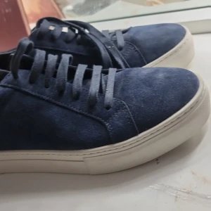 Blå mockasneakers från Vagabond. Orginal pris 1500kr - Snygga sneakers från Vagabond i mörkblå mocka med vita, platta sulor. Skorna har klassisk snörning och en stilren, rund tå. Perfekta för dig som gillar en clean och modern look med lite extra känsla tack vare mockamaterialet.