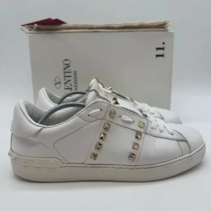 Valentino Garavani vita sneakers - Snygga vita sneakers från Valentino Garavani med ikoniska guldiga nitar längs sidorna. Skorna är i skinn och har en klassisk låg siluett med rund tå och platt sula. Perfekta för dig som vill ha en lyxig och trendig touch till din outfit. Kan gå ner i pris vid snabb affär.